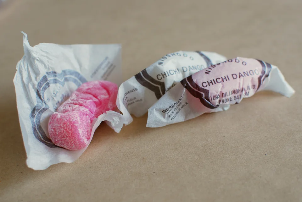 Pink unfilled chichi dango pieces beside Nisshodo Candy Store wrappers.